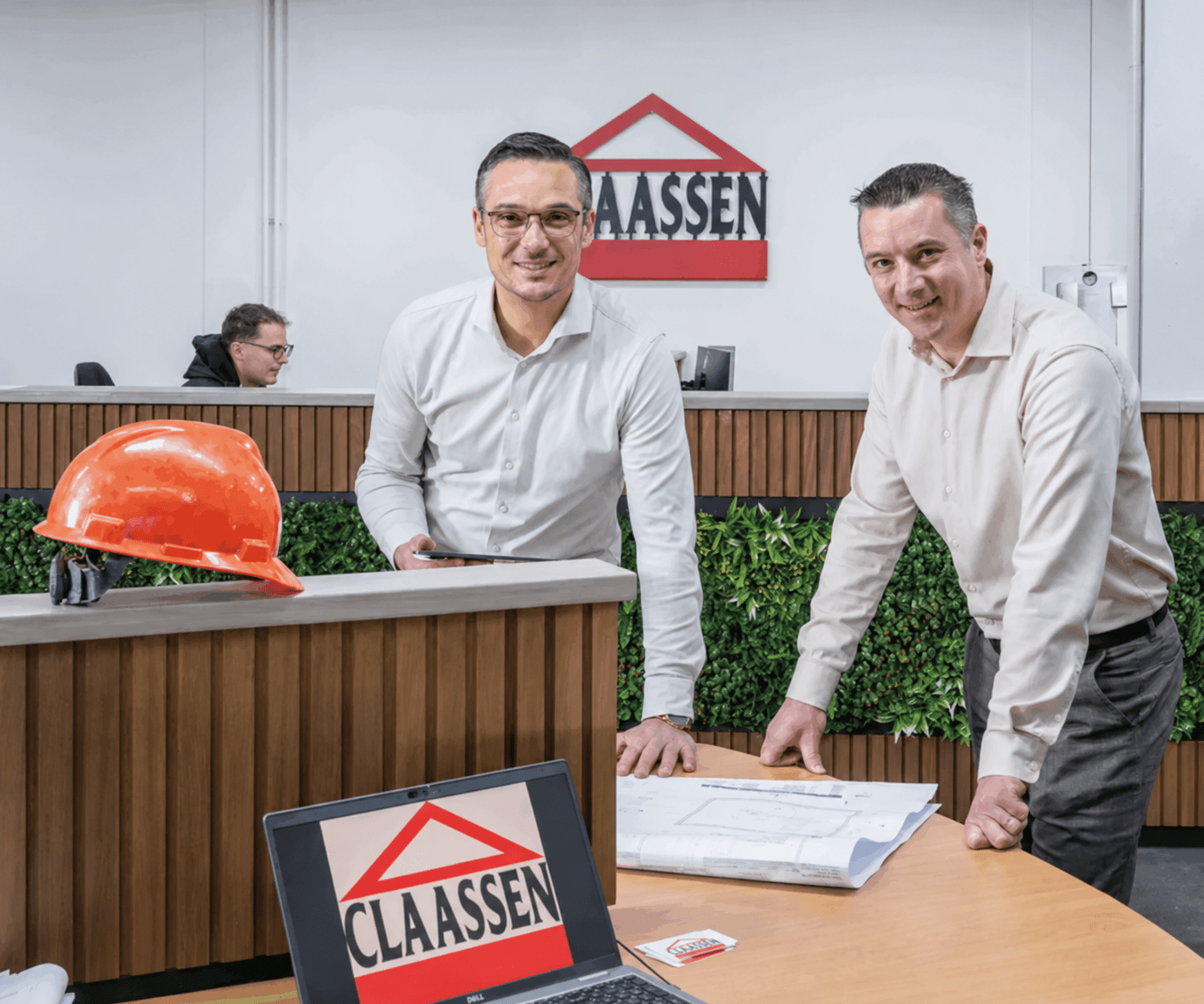 Eigenaren Paul en René Claassen van Claassen Bouw staan in een kantoor te overleggen en kijken lachend in de camera.