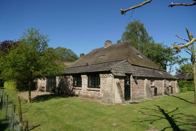Buitenaanzicht van een karakteristieke, gerenoveerde woonboerderij door Claassen Bouw, met een rieten kap, gemetselde gevels met markante betonnen steunberen en donkere raamkozijnen.