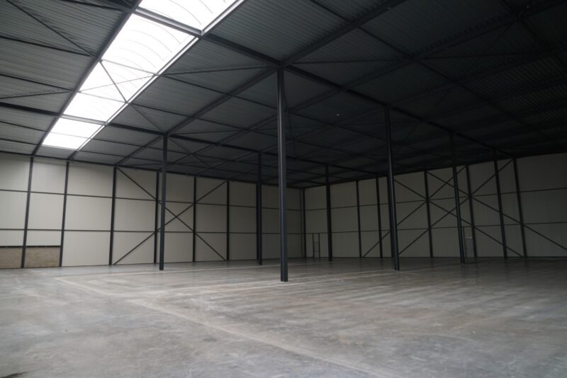 Interieur van een ruime, lege bedrijfshal in Katwijk gebouwd door Claassen Bouw, met een strakke gevlinderde betonvloer, een donkere staalconstructie en veel natuurlijk licht door de grote lichtstraat in het dak.