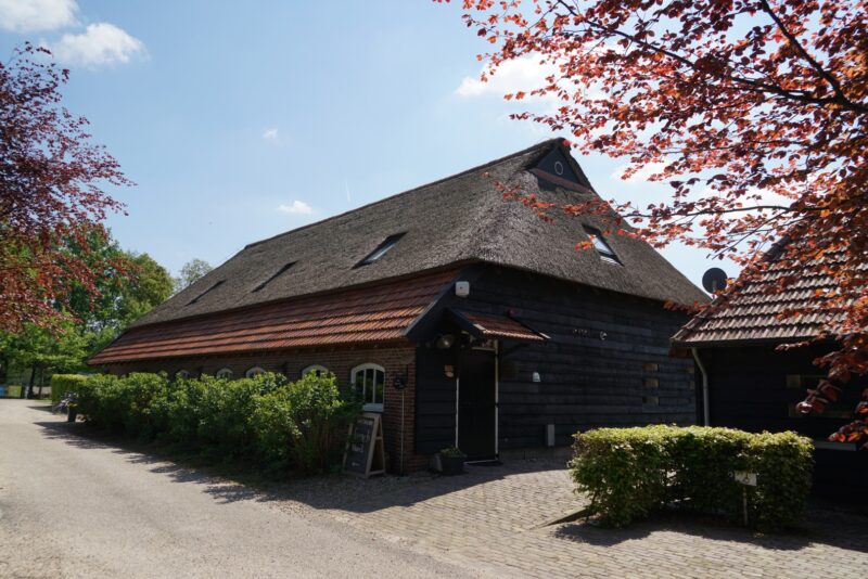 Karakteristiek verbouwde boerderij in Beers, nu dienstdoend als groepsaccommodatie, met zwarte houten wanden, een groot rieten dak en een authentiek pannen dakdeel boven de entree.