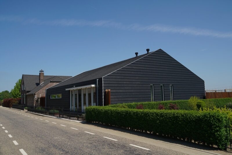 Modern, langwerpig gebouw langs de weg, gerealiseerd door Claassen Bouw, opvallend door de strakke zwarte houten gevelbekleding, een donker pannendak en minimalistische verticale ramen.