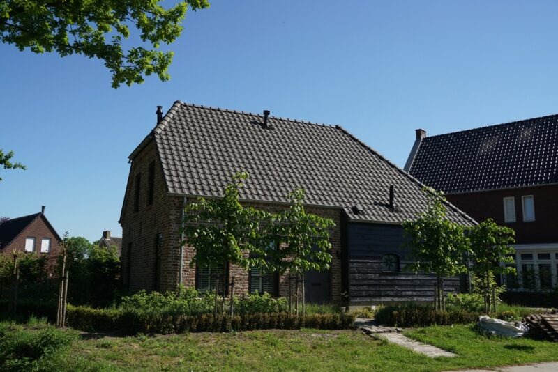 Zijaanzicht van een nieuwbouwwoning van Claassen Bouw, waarbij de naadloze overgang van de robuuste bakstenen gevel naar de moderne, gepotdekselde zwarte houten uitbouw goed zichtbaar is.
