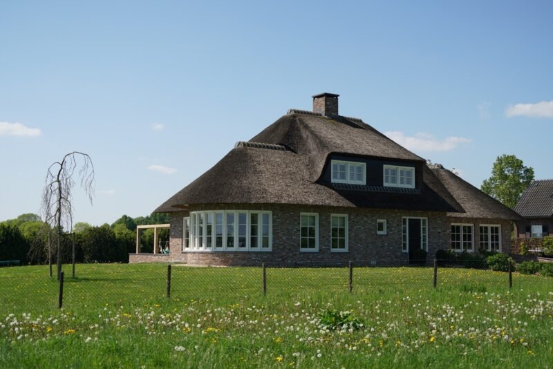 Vrijstaande nieuwbouwwoning van Claassen Bouw in landelijke stijl met een rieten kap, bakstenen gevels en grote witte raampartijen, gelegen aan een groen weiland in Beers.