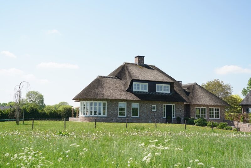 Vooraanzicht van een rietgedekte landelijke nieuwbouwwoning in Beers, gebouwd door Claassen Bouw, met een ronde erker, dakkapel en een uitgestrekt grasveld op de voorgrond.