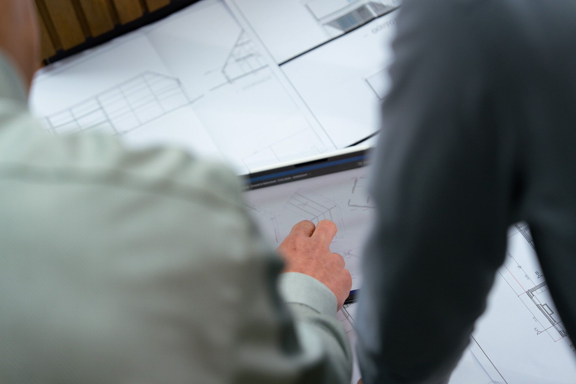 Close-up van René en Paul Claassen tijdens een projectoverleg, waarbij over de schouder wordt meegekeken naar een hand die details aanwijst op een digitaal ontwerp op een tablet, met papieren bouwtekeningen op de achtergrond.