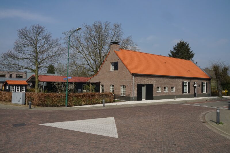 Straataanzicht van een langgerekte, gerenoveerde woonboerderij in Cuijk, vakkundig verbouwd door Claassen Bouw, met een klassieke bakstenen gevel, donkere luiken en een vernieuwd rood pannendak.
