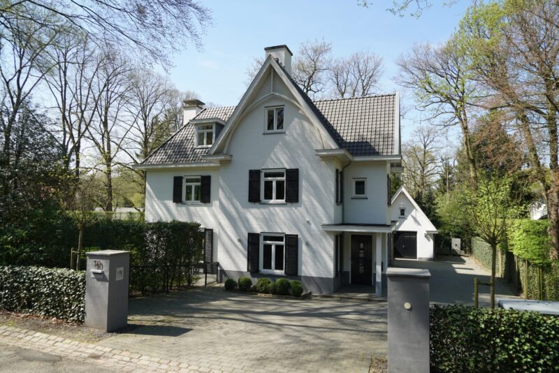 Vooraanzicht van een statige, wit geschilderde villa aan de Torenweg in Nijmegen, gebouwd door Claassen Bouw, met donkere luiken, een pannendak en een ruime oprit met strakke toegangspilaren.