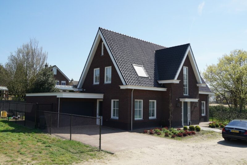 Zijaanzicht van een vrijstaande donkere stenen nieuwbouwwoning in Molenhoek, gebouwd door Claassen Bouw, met een aangebouwde garage voorzien van een plat dak en een bestrate oprit.