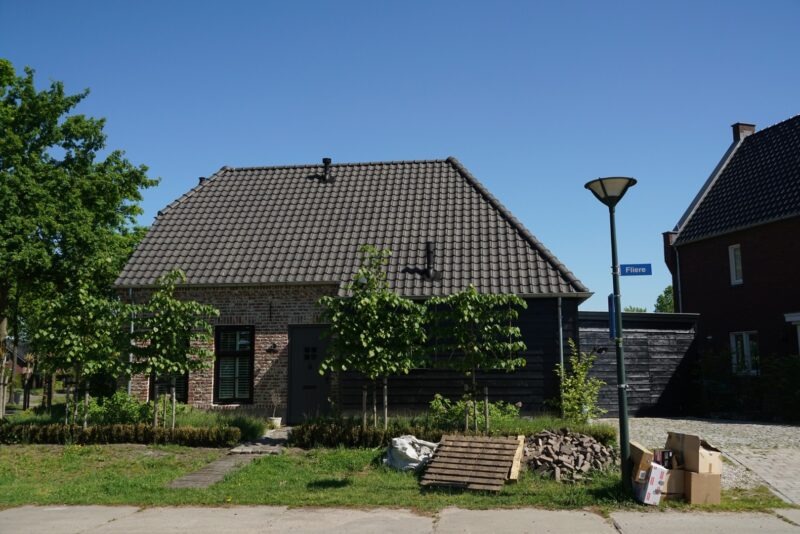 Straataanzicht van een door Claassen Bouw gerealiseerde woning met een bakstenen gevel, een zwart houten middengedeelte en een aangebouwde houten garage, gefotografeerd op een zonnige dag.
