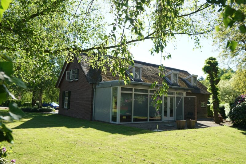 Landelijke woonboerderij met rieten kap en dakkapellen, waaraan Claassen Bouw een strakke, moderne glazen aanbouw heeft gerealiseerd voor extra leefruimte en lichtinval.