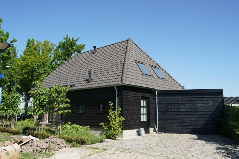 Zwarte houten zijgevel en aangebouwde garage van een woning gerealiseerd door Claassen Bouw, voorzien van dakramen in het donkere pannendak en een oprit bestraat met kinderkopjes.